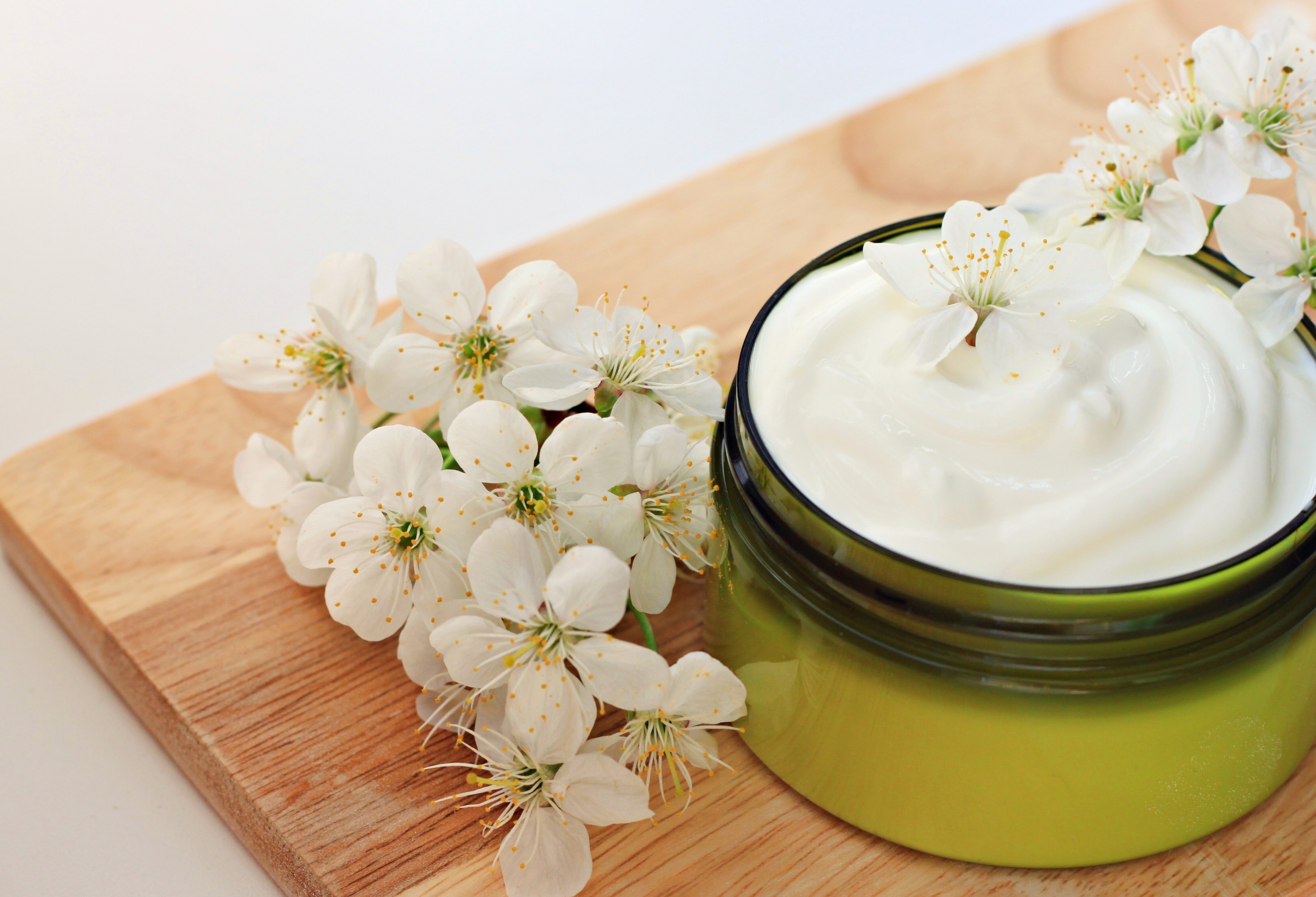 Glas mit pflanzlicher Feuchtigkeitscreme umgeben von frischen Frühlingsblumen